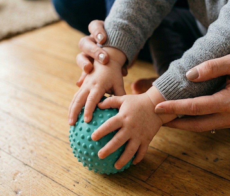 Therapist and child's hands working together with a sensory ball during physiotherapy