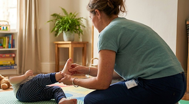 Physiotherapist supporting a baby's foot and ankle during a home therapy session